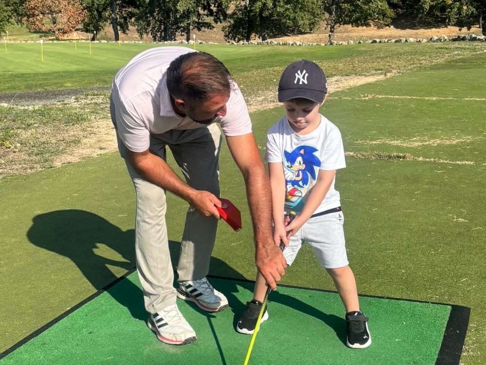 Éric Poujeol guide un enfant du Baby Golf pour son premier swing, sur le practice du Golf du Claux Amic